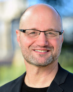 Color head shot of Michael L. Royce. Michael wears a black shirt and jacket and has a close cropped beard and wears glasses.