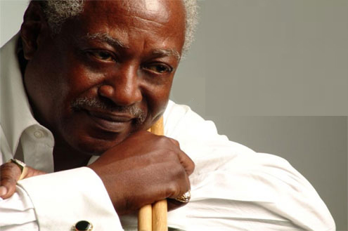 Headshot of Roger Humphries. Mr. Humphries wears a white shirt with French cuffs. His chin leans on one hand which holds a pair of drum sticks. Mr. Humphries is a mature Black man.