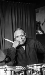Black and white photo of Billy Hart seated behind a drum kit.