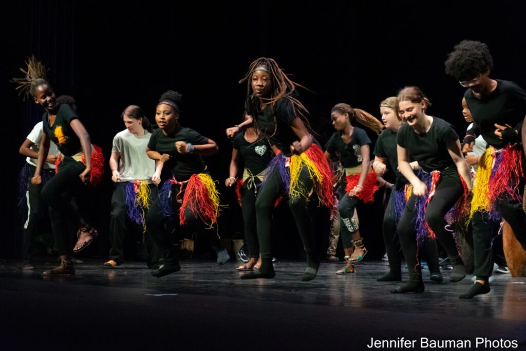 Color photo of a group of students dancing joyously onstage led by professional dancers.