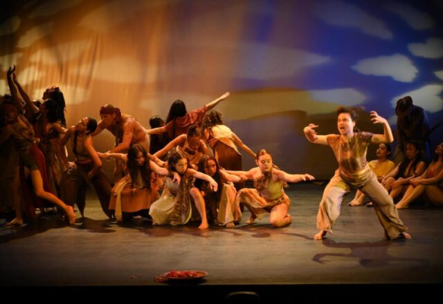 Dancers in earth tones form a tableau on a stage. Sime crouch while other move forward.