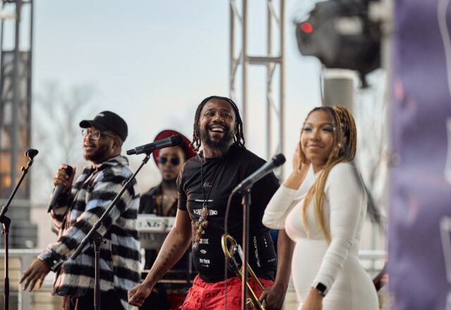 A group of musicians and vocalists perform on an outdoor stage.